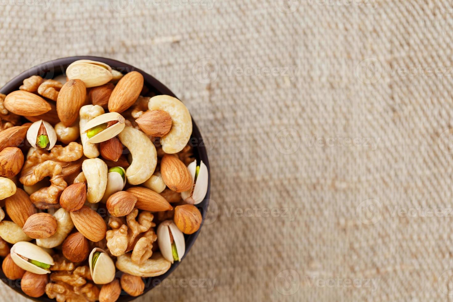 Mix of different nuts in a wooden cup against the background of fabric from burlap. Nuts as structure and background, macro. Top view. photo