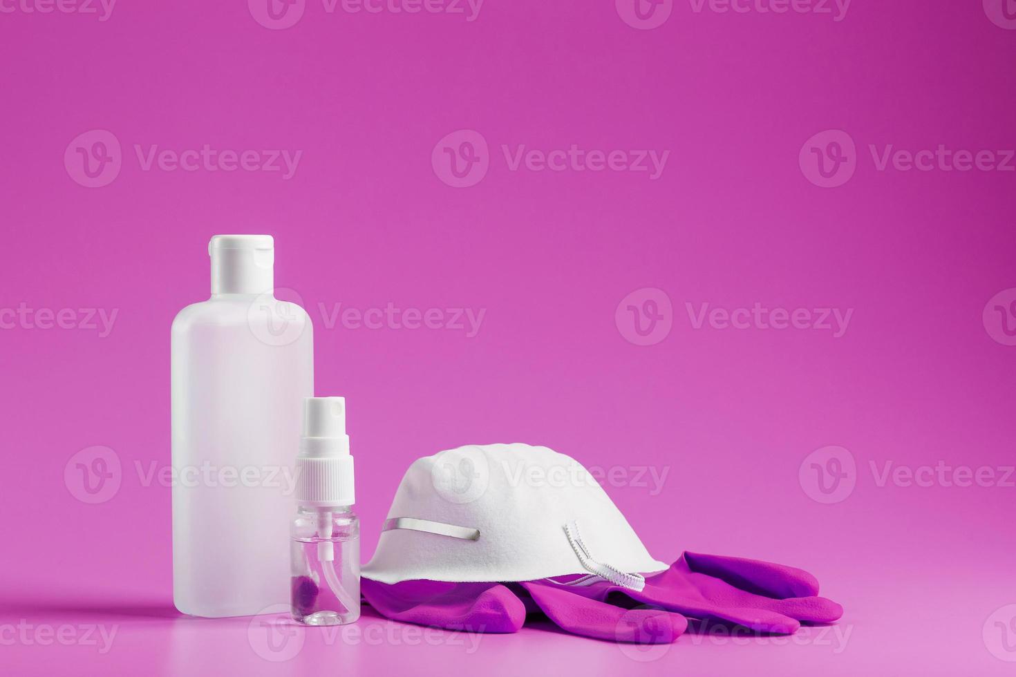 kit de protección antivirus sobre fondo rosa, máscara, guantes de goma, botellas de desinfectante para manos, gel antiséptico. aislar foto