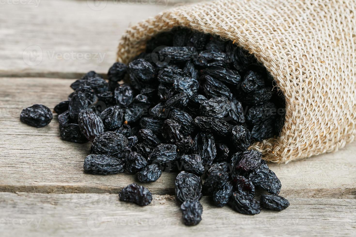 Black raisins in burlap bag over wooden gray table photo