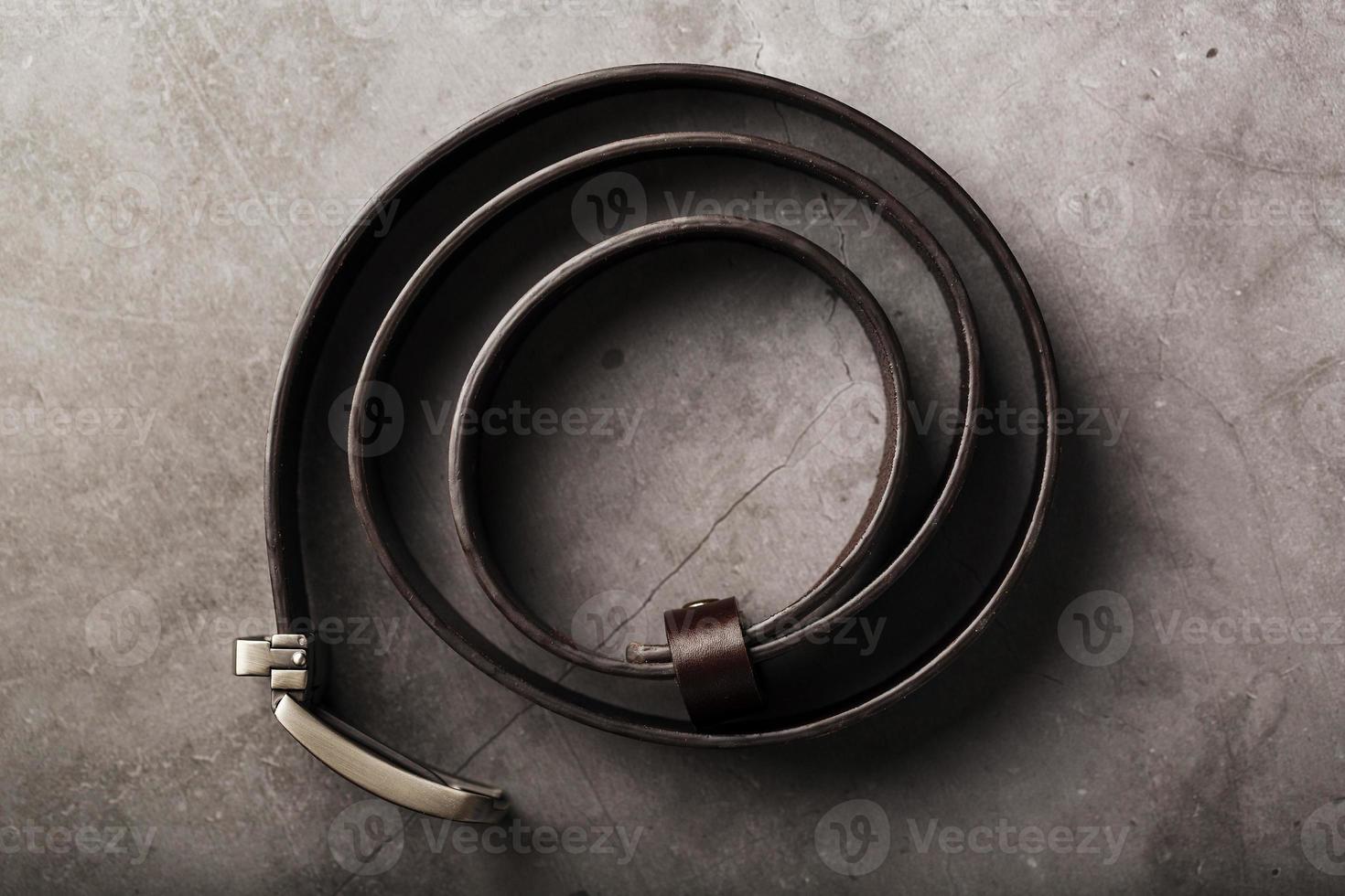 cinturón marrón de moda para hombres hecho de cuero genuino con una hebilla de metal claro sobre un fondo oscuro. cuero genuino, hecho a mano foto