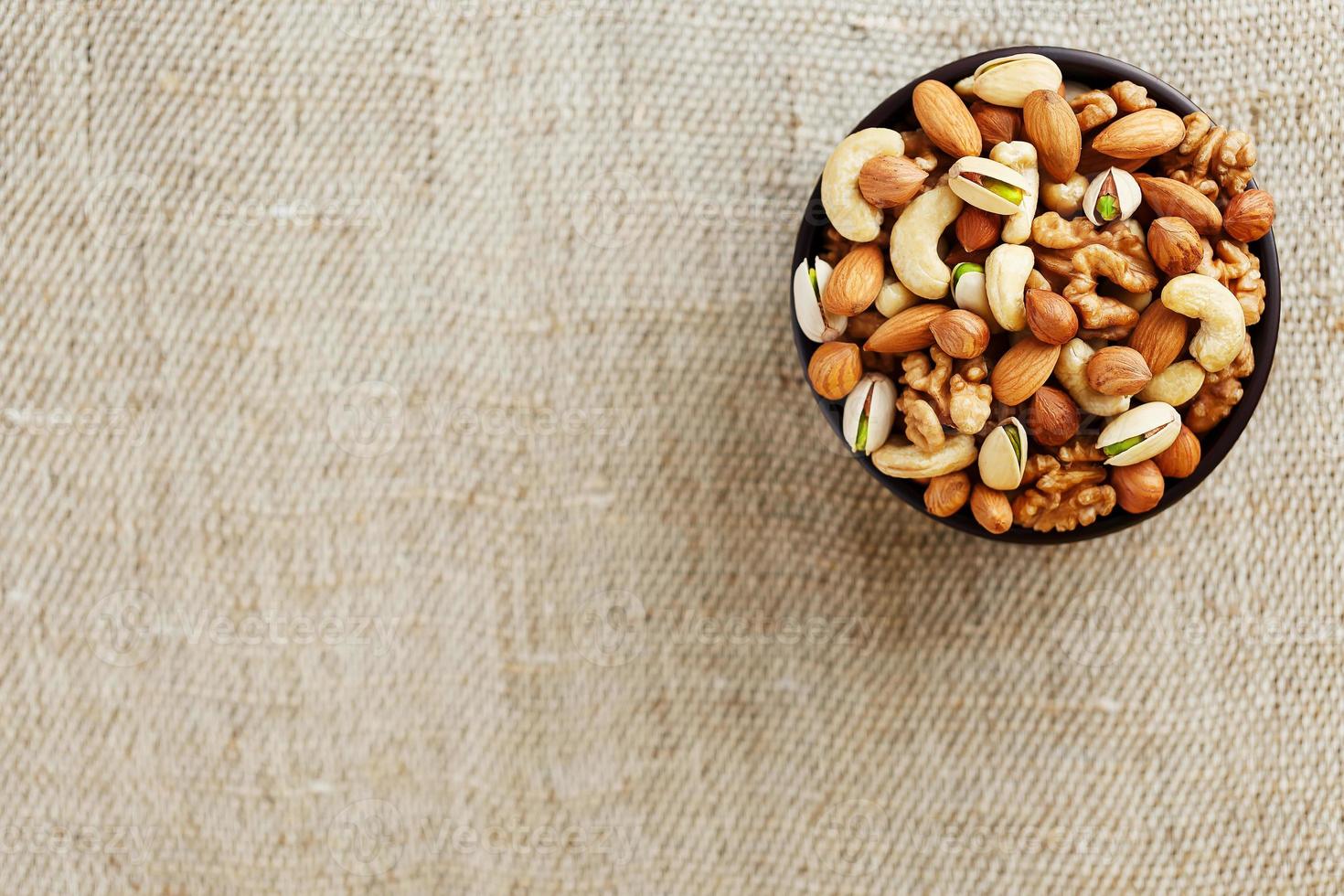 Mix of different nuts in a wooden cup against the background of fabric from burlap. Nuts as structure and background, macro. Top view. photo