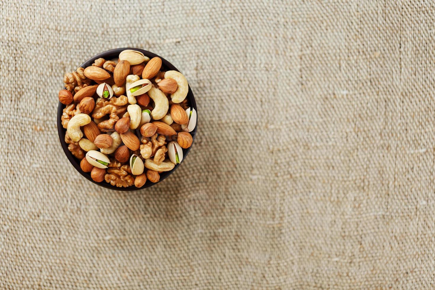 Mix of different nuts in a wooden cup against the background of fabric from burlap. Nuts as structure and background, macro. Top view. photo