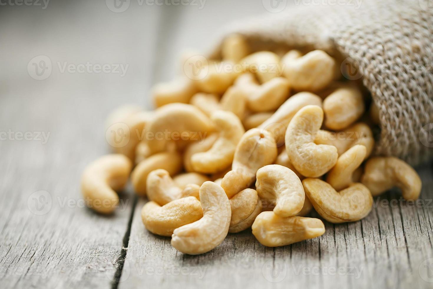 Cashew nuts in burlap bag on wooden gray background . Healthy food photo