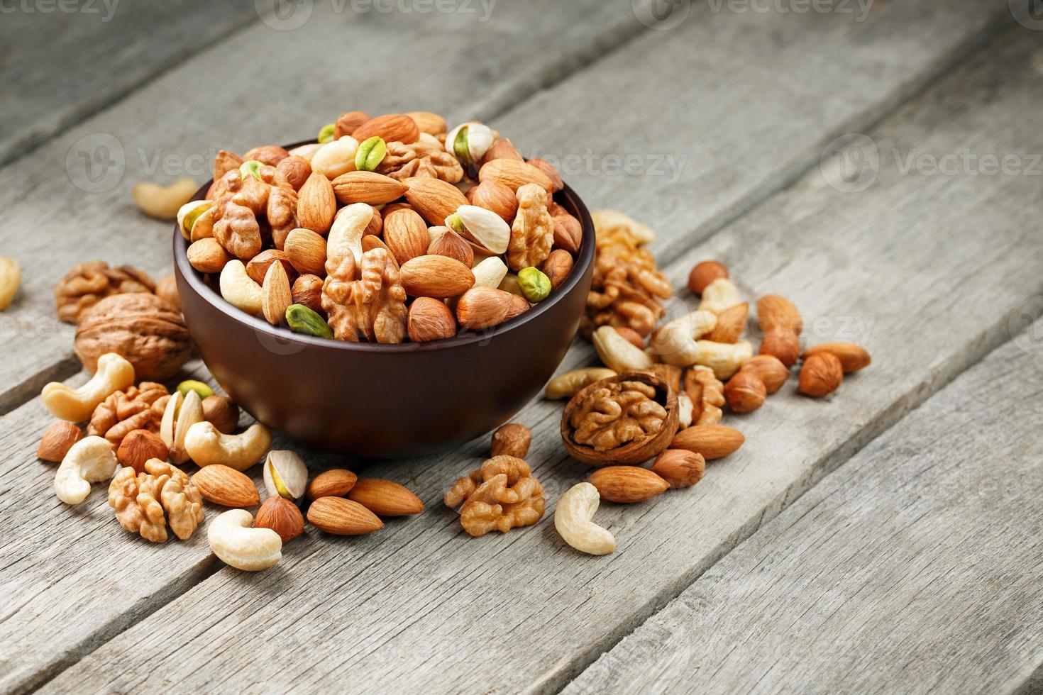 Wooden bowl with mixed nuts on a wooden gray background. Walnut, pistachios, almonds, hazelnuts and cashews, walnut. photo