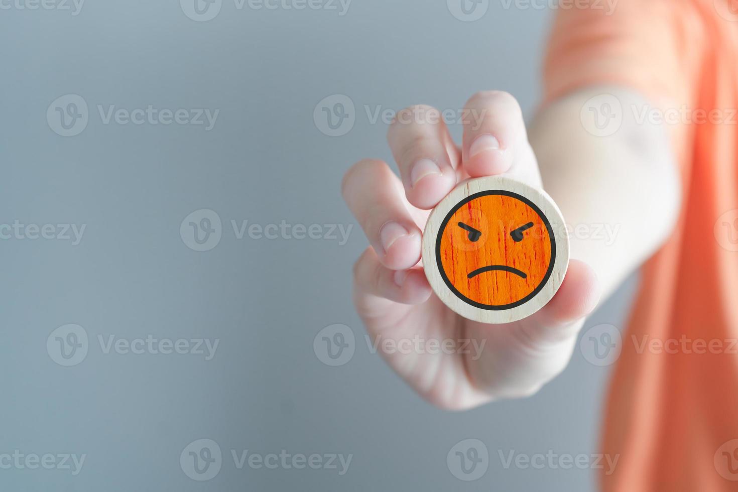 Hand showing angry face on wooden circle. Unhappy, Negative, Mental health assessment, World mental health day, Feedback, Satisfaction, Customer service review concept. photo