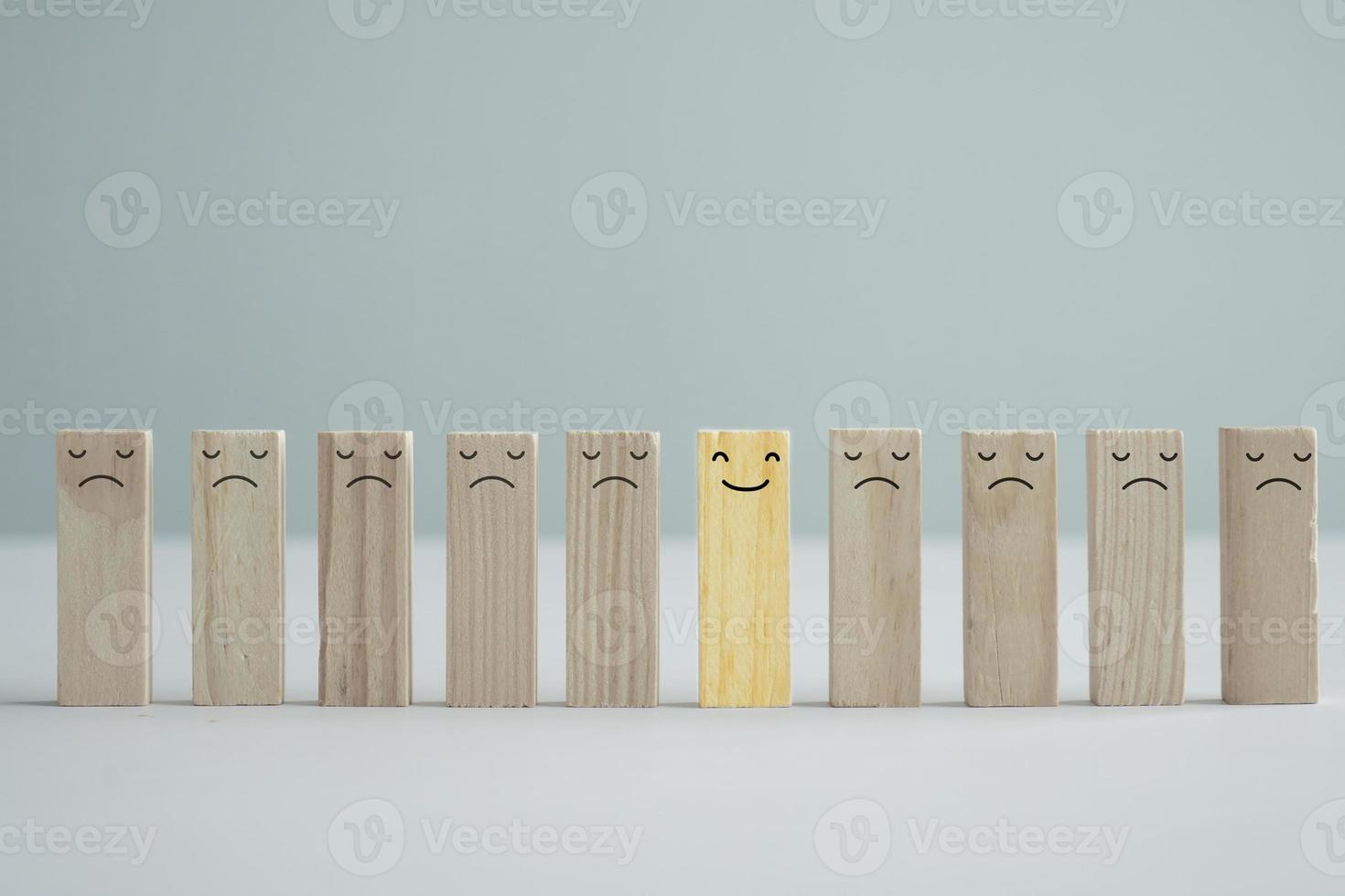 Happy smiling face among unhappy faces on wooden blocks. Positive thinking, Unique, Individuality, Difference, Emotion, Positive thinking, Mental health assessment, World mental health day concept. photo