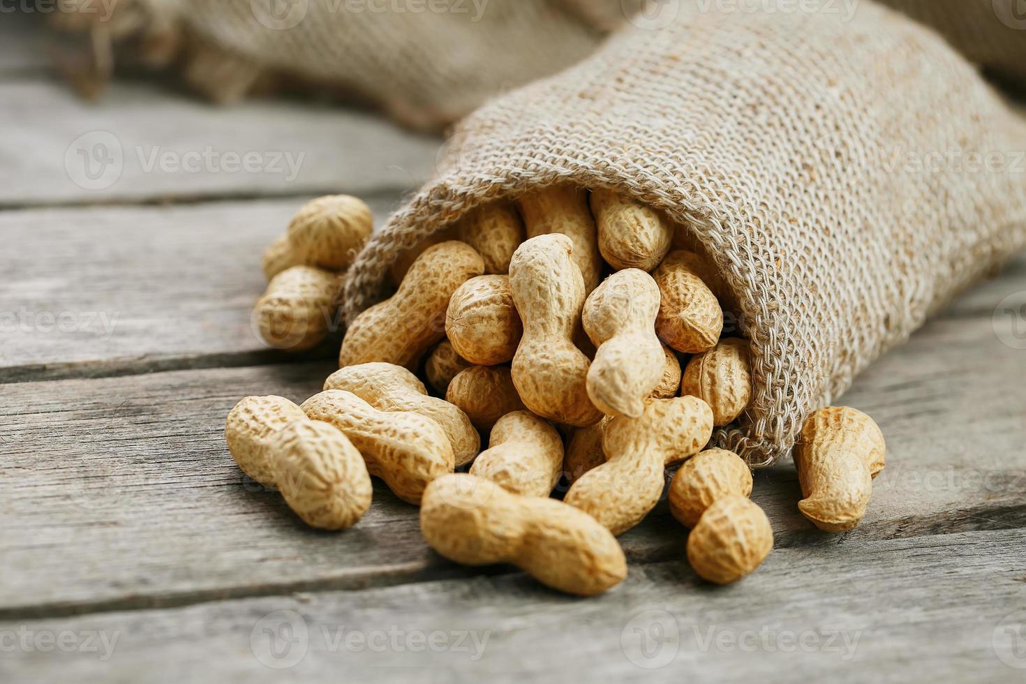 Peanuts in a miniature burlap bag on old, gray wooden surface photo