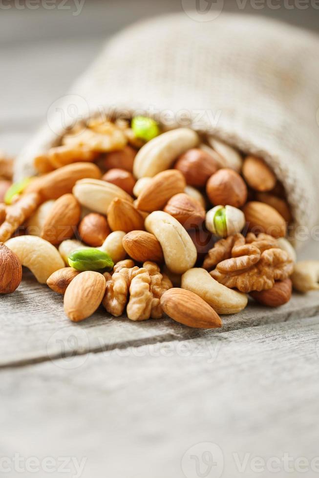 Mix of different nuts in a wooden cup against the background of fabric from burlap. Nuts as structure and background, macro. Top view. photo