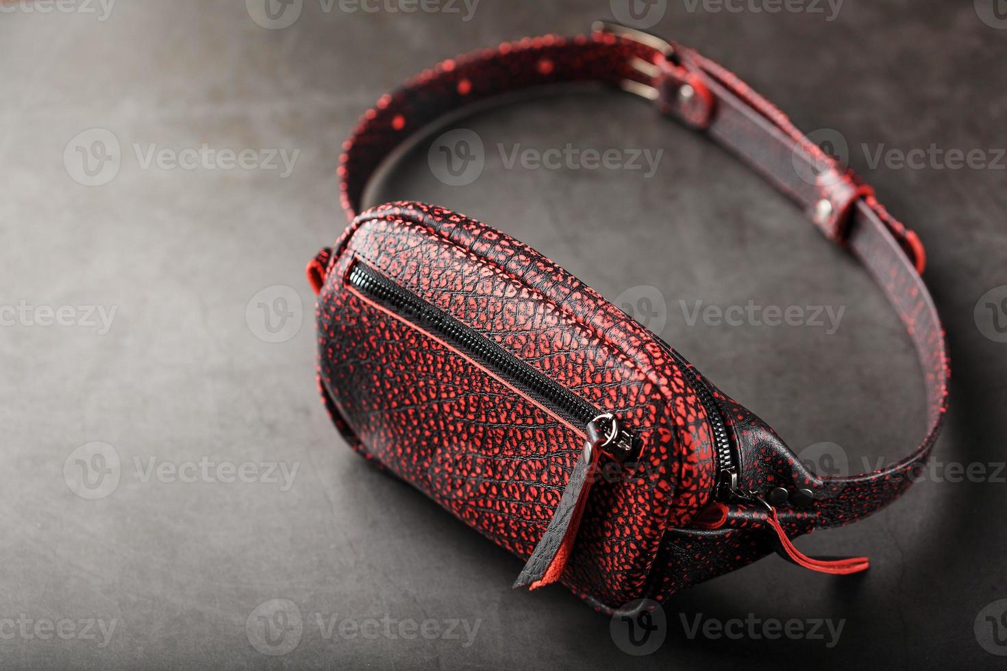 Belt bag made of textured, spotty black and red leather on a stone dark background. Elegant black and red bag with a zipper. Genuine leather, handmade photo