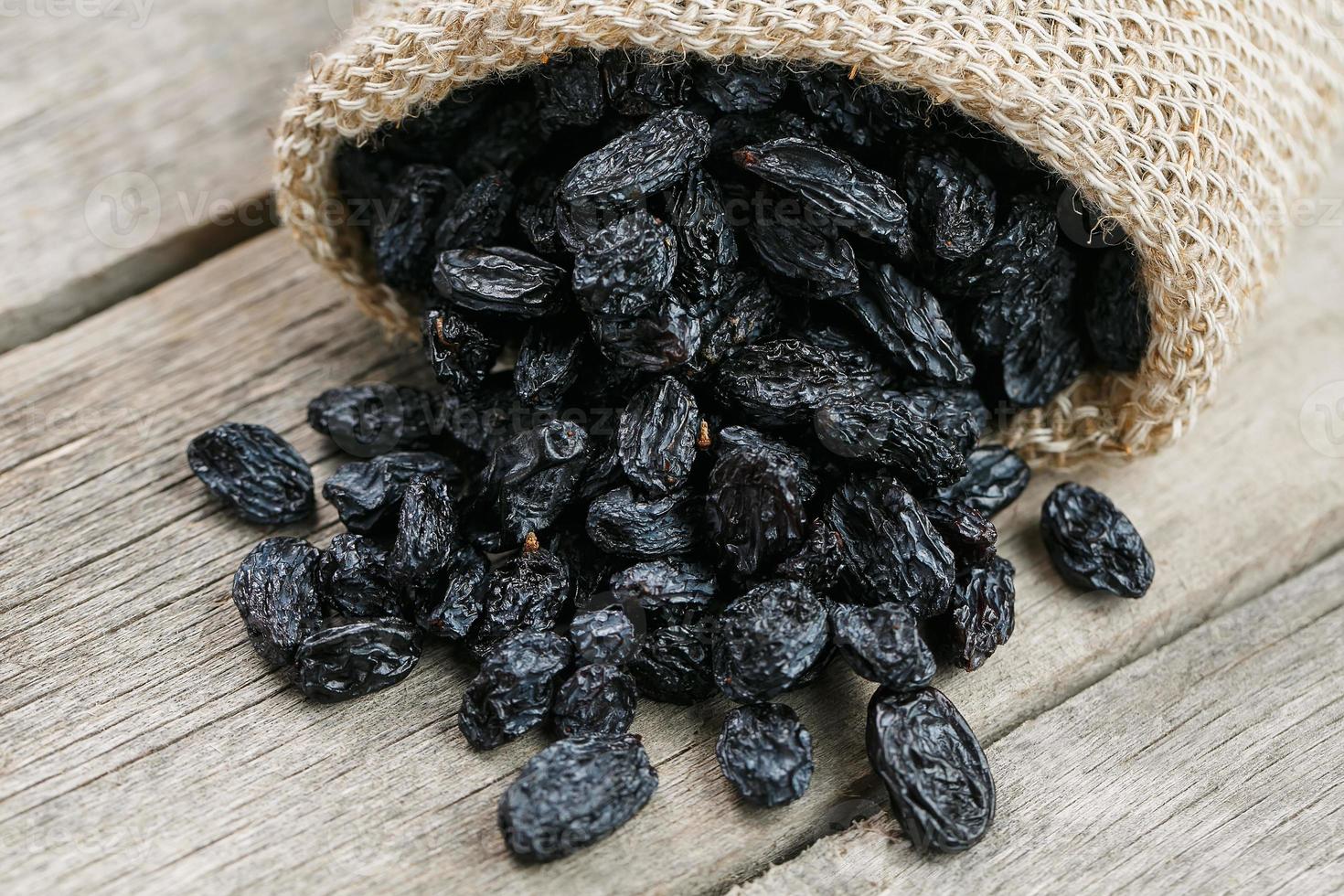 Black raisins in burlap bag over wooden gray table photo