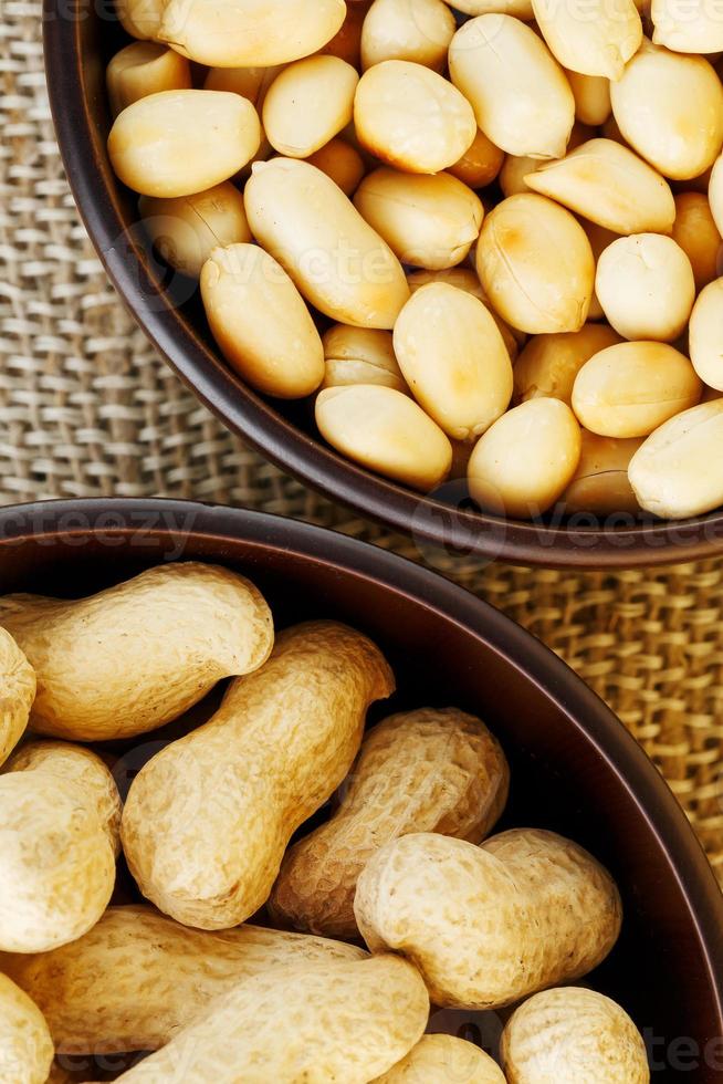 Peanuts in the shell and peeled close-up in cups. Roasted peanuts in their shells and peeled against a brown cloth. photo