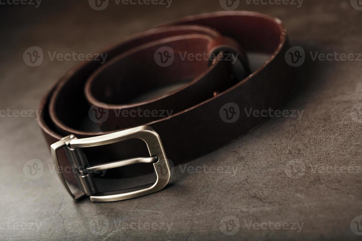 Fashionable men's brown belt made of genuine leather with a light metal buckle on a dark background. Genuine leather, handmade photo