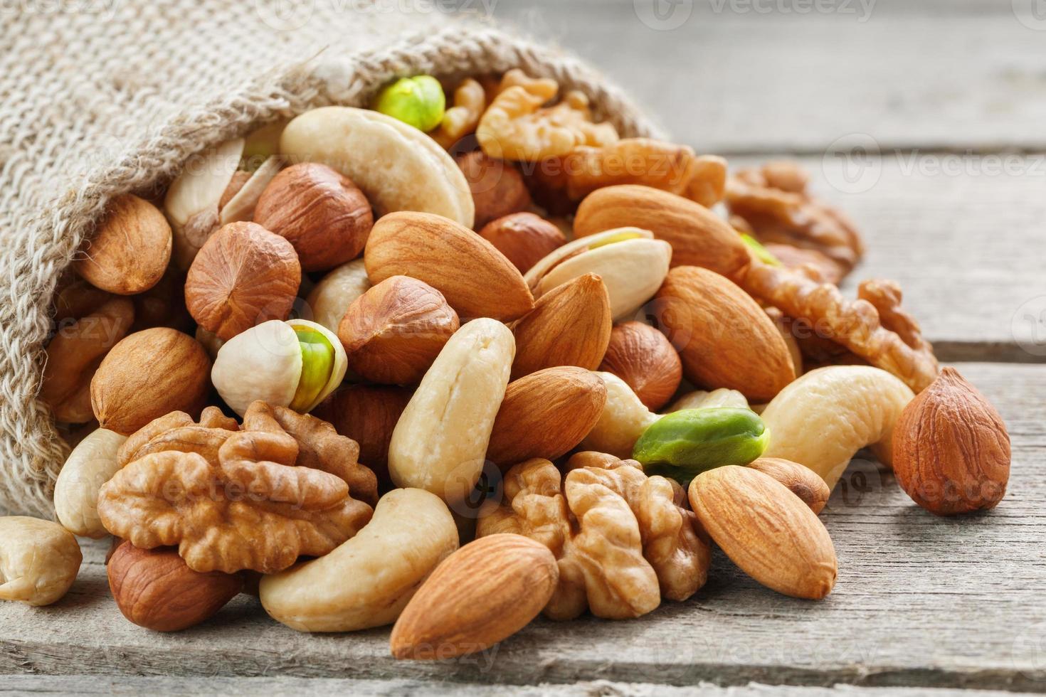 Mix of different nuts in a wooden cup against the background of fabric from burlap. Nuts as structure and background, macro. Top view. photo