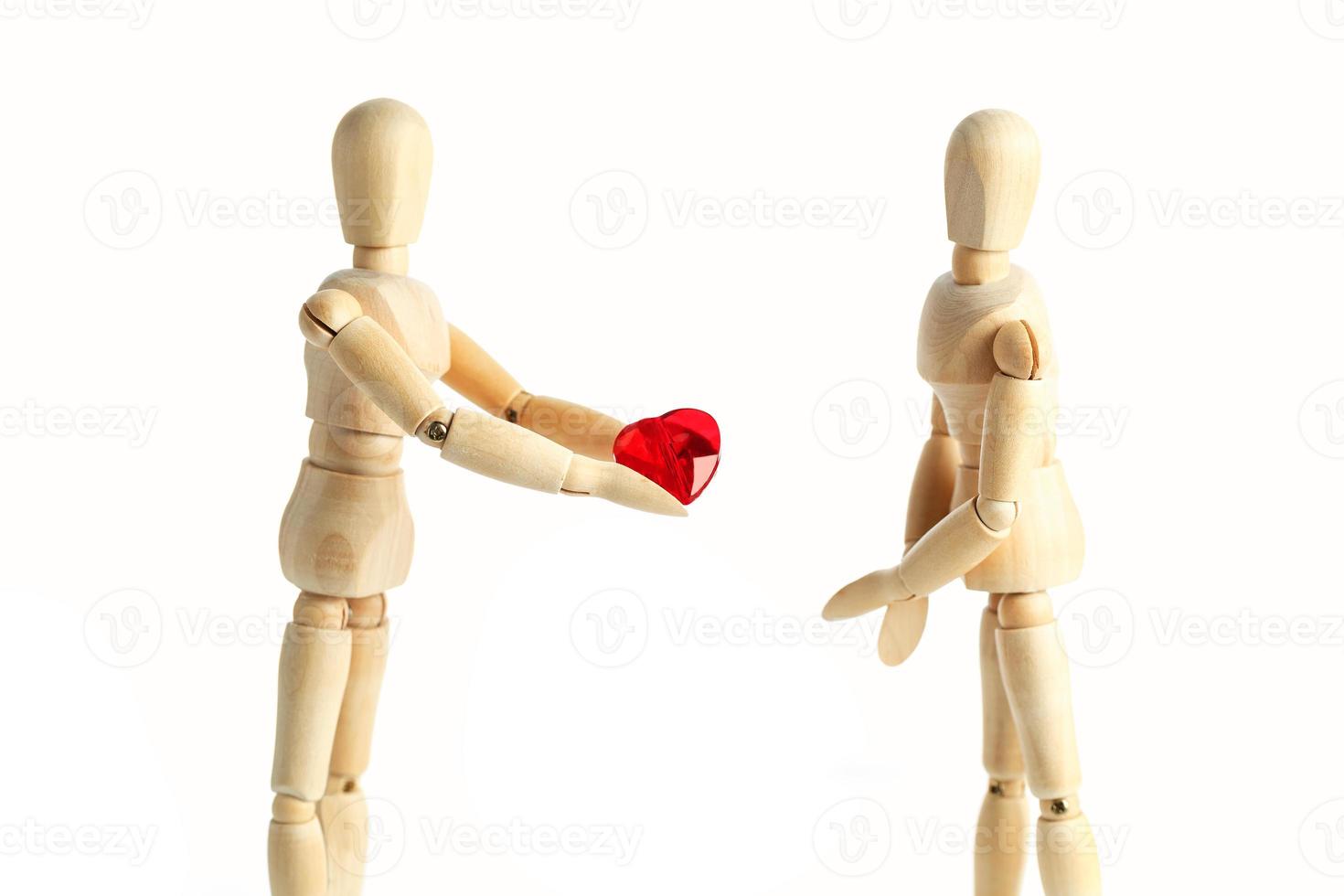 Two wooden figures of a dummy, give a red heart, isolated on a white background - pictures of the theme concepts Love and Valentine's Day. photo
