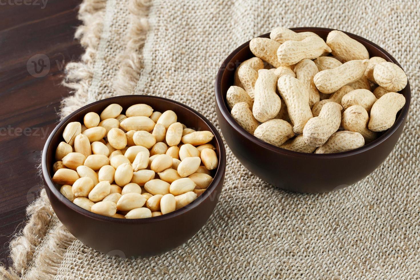 Peanuts in the shell and peeled close-up in cups. Roasted peanuts in their shells and peeled against a brown cloth. photo