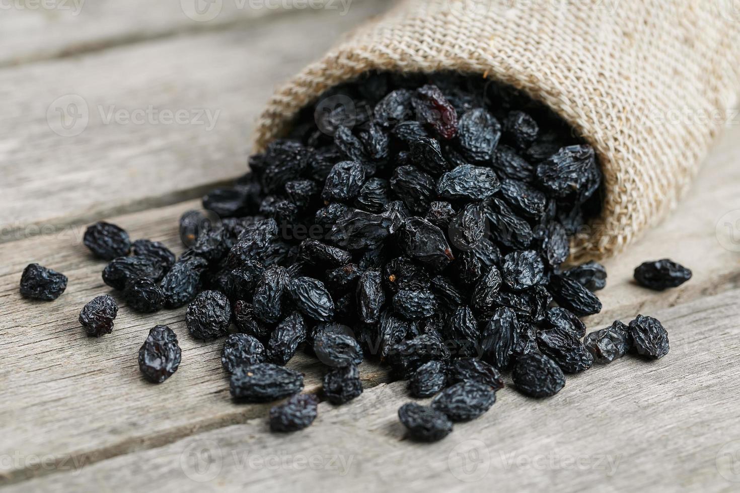 Black raisins in burlap bag over wooden gray table photo