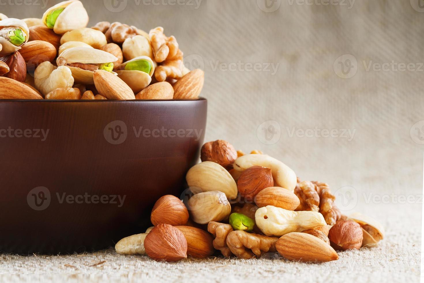 Mix of different nuts in a wooden cup against the background of fabric from burlap. Nuts as structure and background, macro. Top view. photo