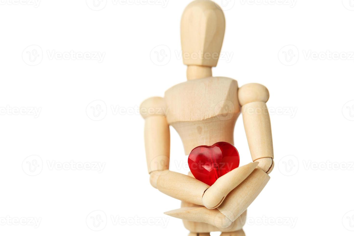 The wooden figure of a man holds in his hands a red heart on a white background. Gives the heart photo