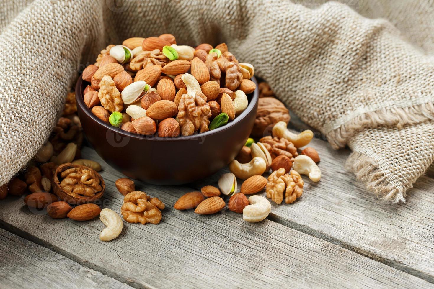 Wooden bowl with nuts on a wooden background, near a bag from burlap. photo