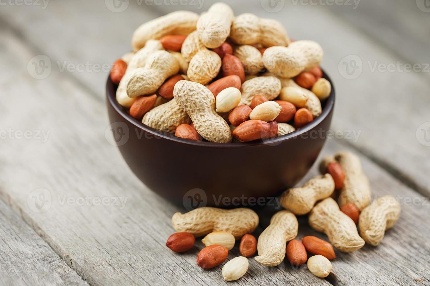 Roasted peanuts in the shell and peeled in a cup, against a gray wooden table photo