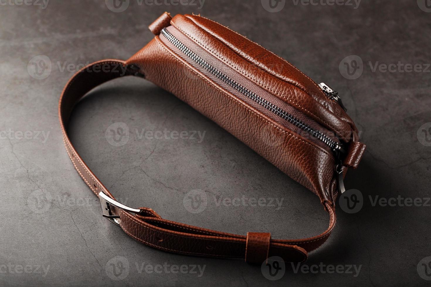 A brown belt bag made of textured brown leather on a black stone background. Elegant fanny pack brown bag with a zipper photo