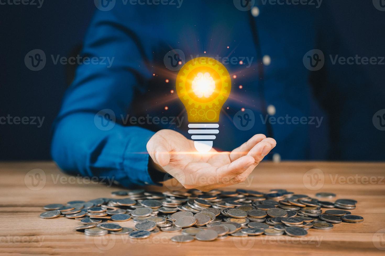 Man holding a glowing abstract light bulb with pile money cions on a wooden table, business problem solving ideas and creative marketing ideas Inventing and learning new things. photo