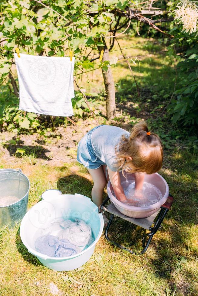 la niña de preescolar ayuda con la lavandería. niño lava ropa en el jardín foto