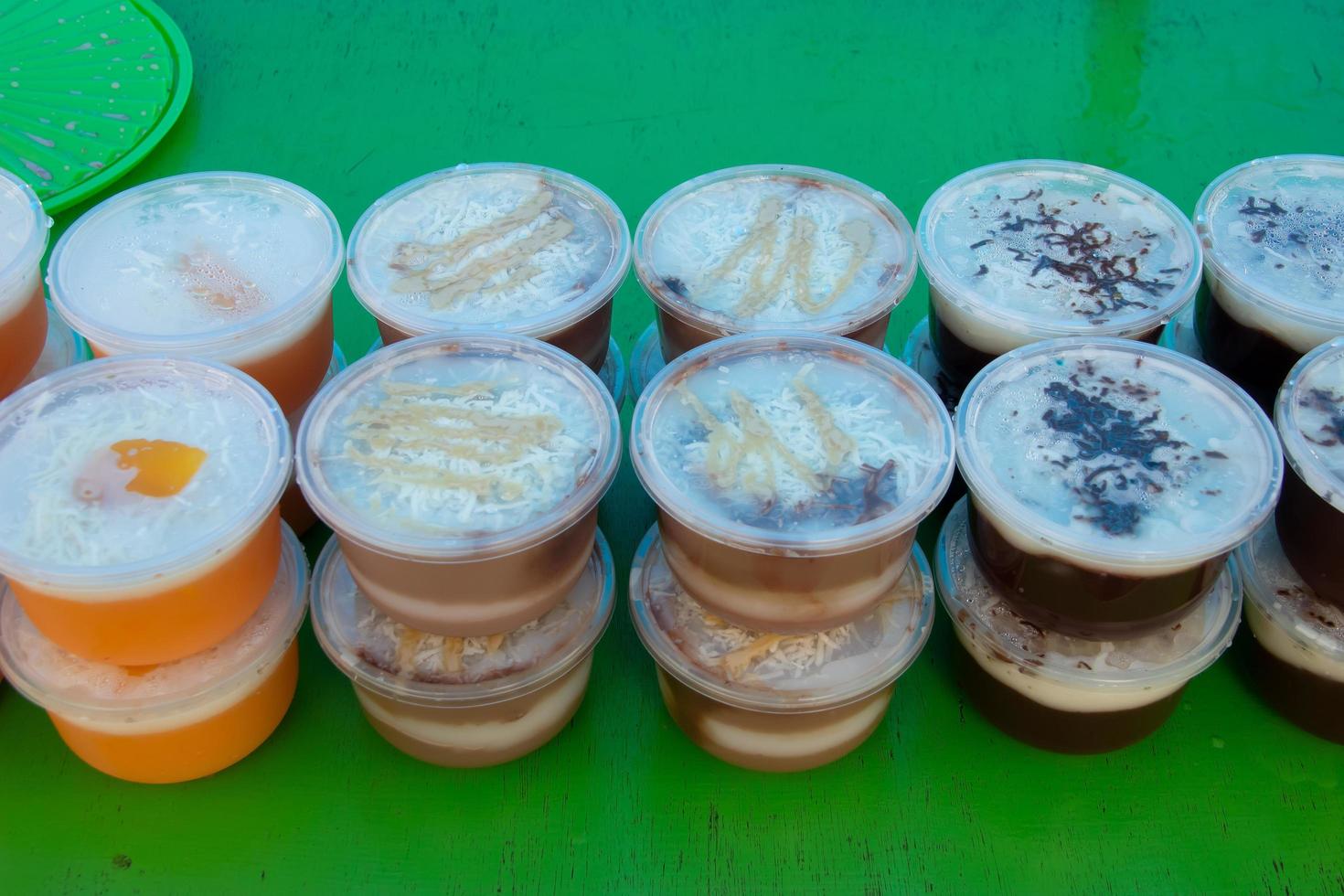 Puddings in plastic containers are placed on a green table, sold by street vendors photo