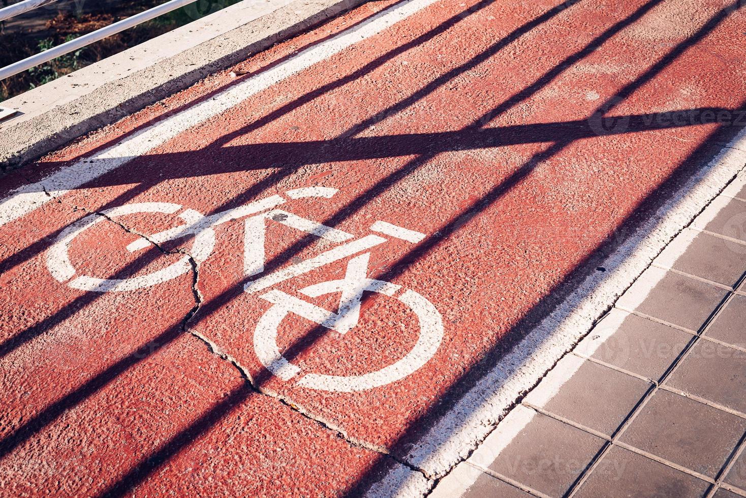 Bicycle sign on a red bike path under a shadow of a fence photo