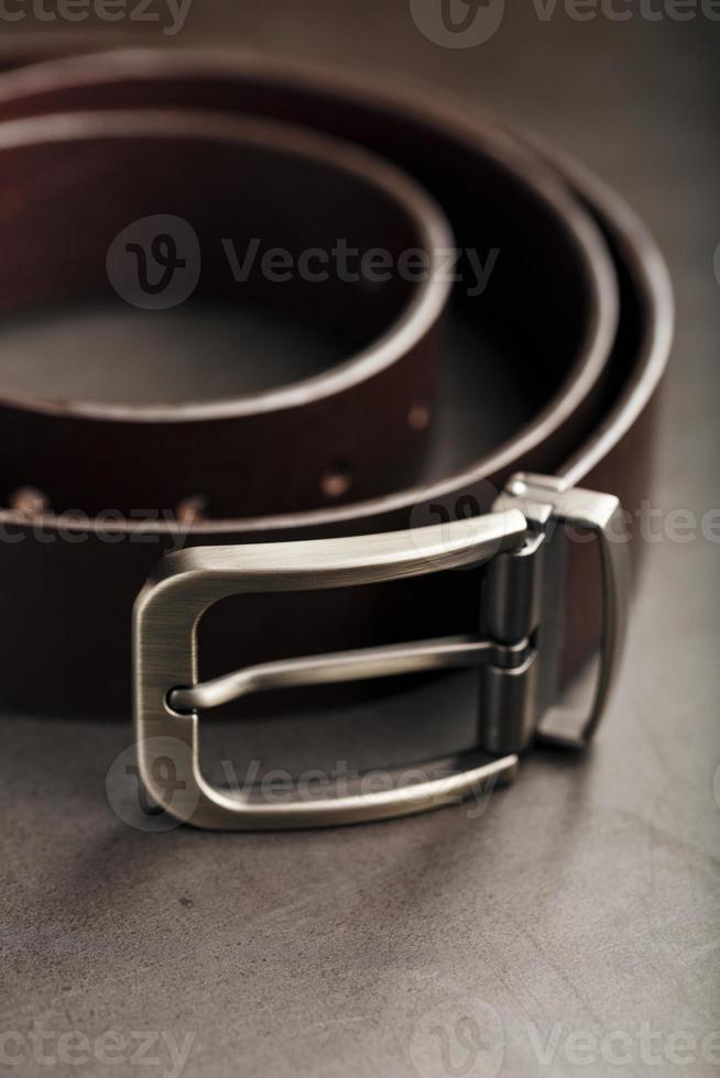 cinturón marrón de moda para hombres hecho de cuero genuino con una hebilla de metal claro sobre un fondo oscuro. cuero genuino, hecho a mano foto