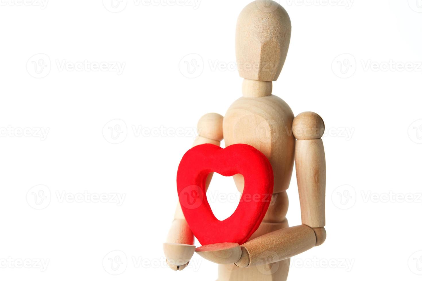 la figura de madera de un hombre sostiene en sus manos un corazón rojo sobre un fondo blanco. da el corazón foto