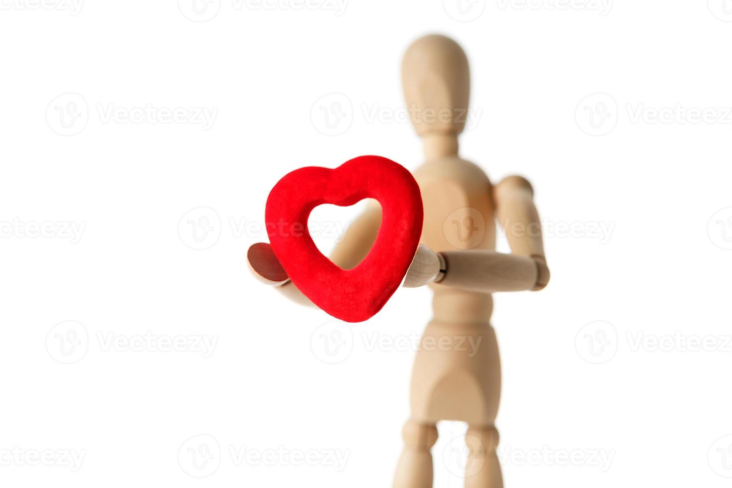 The wooden figure of a man holds in his hands a red heart on a white background. Gives the heart photo