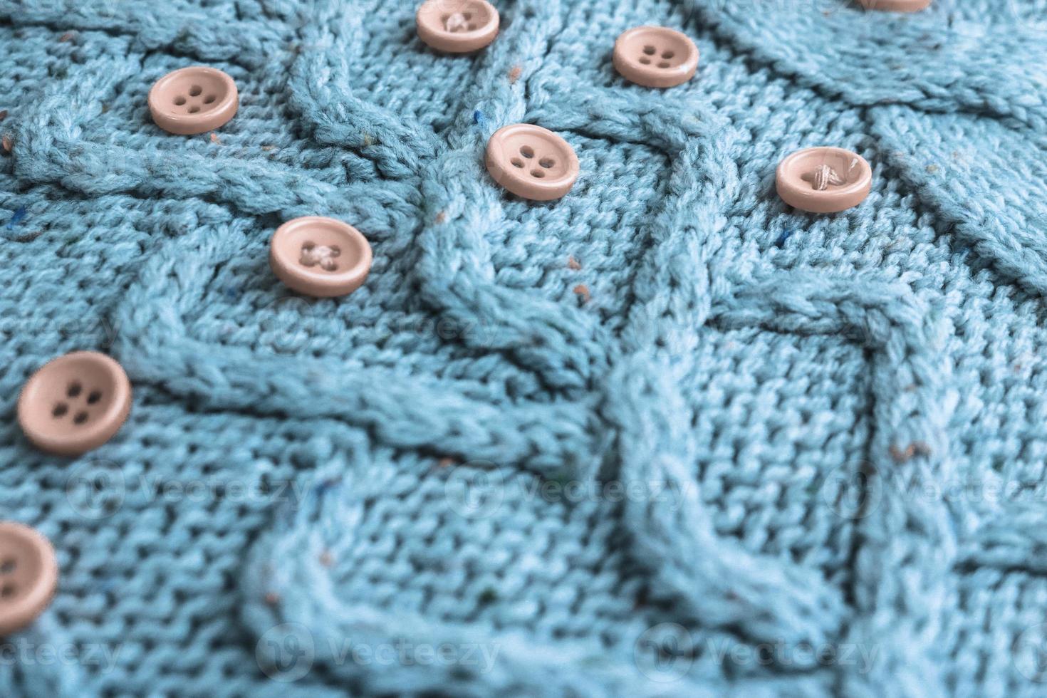 Beautiful texture of a soft warm natural sweater with a knitted pattern of yarn and red small round buttons for sewing. The background photo