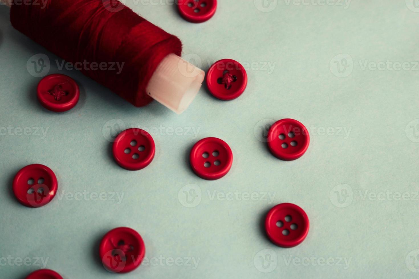 Beautiful texture with lots of round red buttons for sewing, needlework and a coil of thread. Copy space. Flat lay. Blue background photo