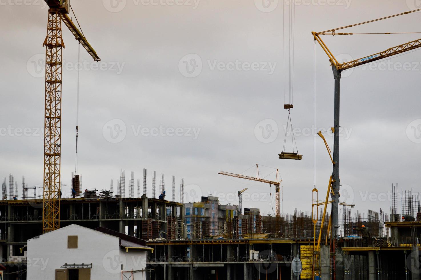 los constructores masculinos que trabajan están trabajando en el techo de una gran casa monolítica, un edificio y un nuevo edificio en construcción. construcción del edificio en el nuevo micro distrito de la gran ciudad foto