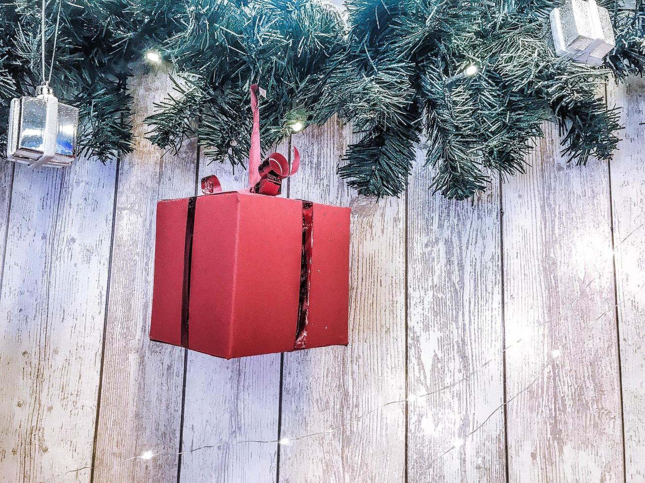Small cute red festive gift boxes, Christmas, New Year's decoration on the background of green Christmas-tree branches with needles and glowing garlands on wooden vertical boards with seams photo