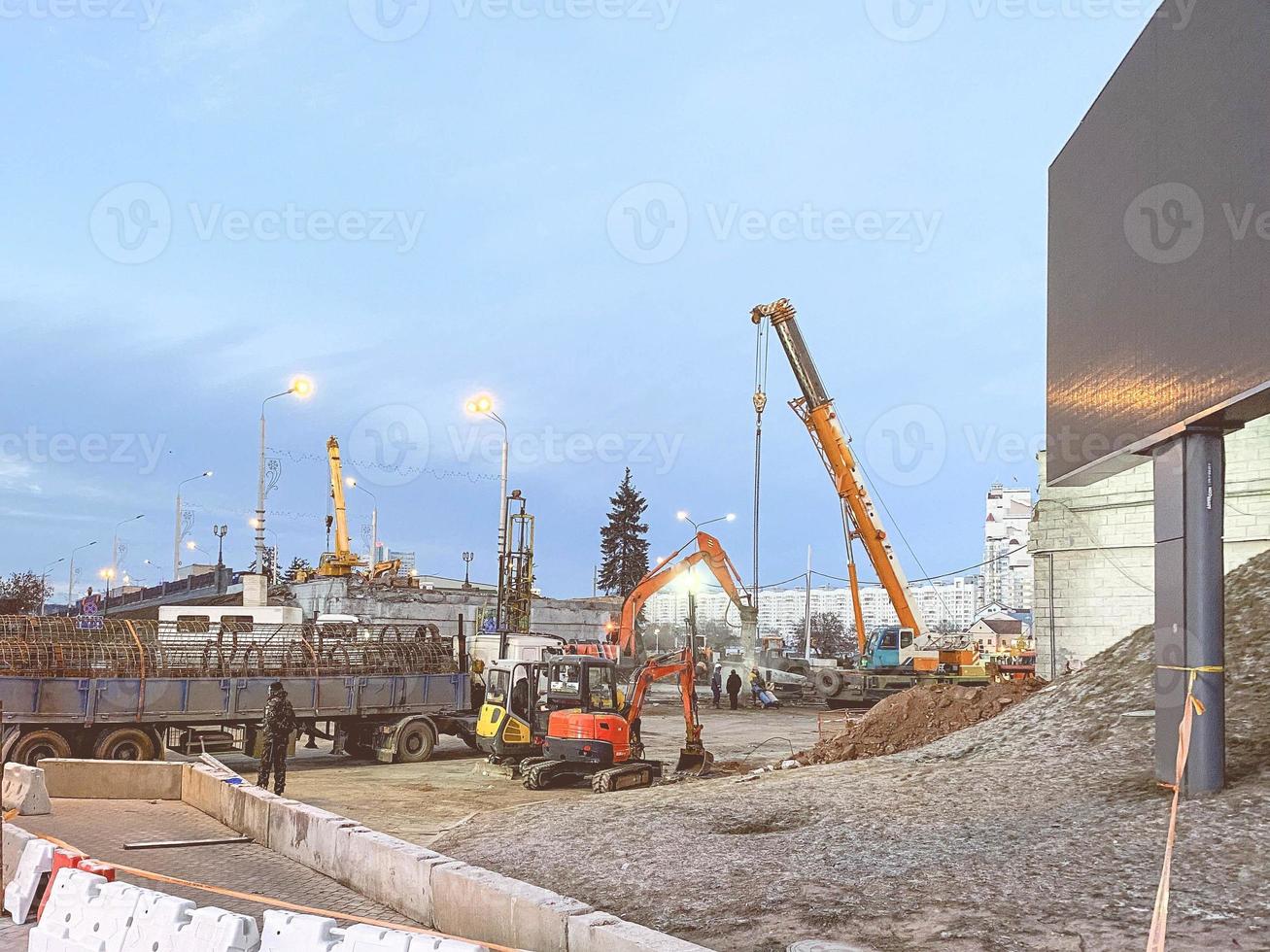 construction of a broken bridge on a busy road. heavy trucks brought a metal frame for the overpass. an orange crane carries blocks to a height for construction photo