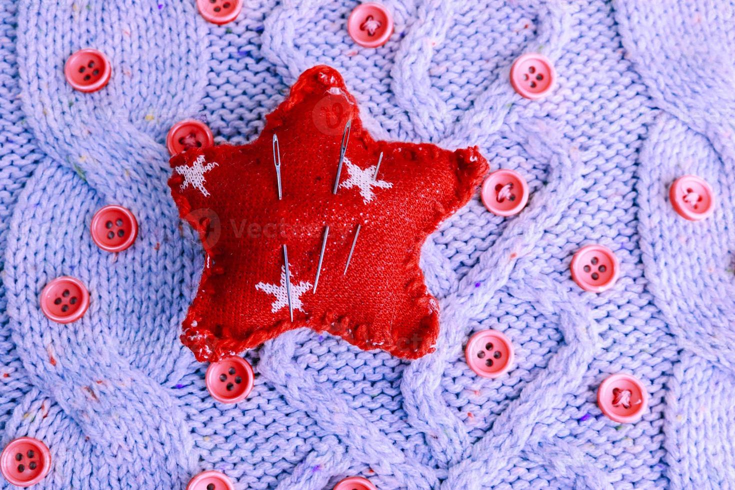 Beautiful texture of a soft warm natural sweater, knitted fabrics and red small round buttons for sewing and a needle pad. Flat lay. The background photo