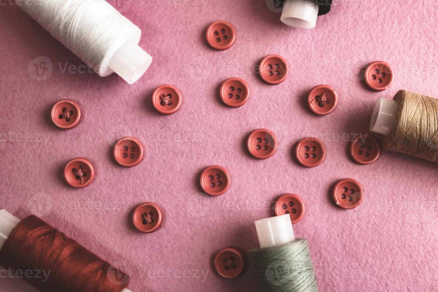 Beautiful frame with a lot of round red buttons for sewing, needlework and skeins of spools of thread. Copy space. Flat lay. Purple pink background photo