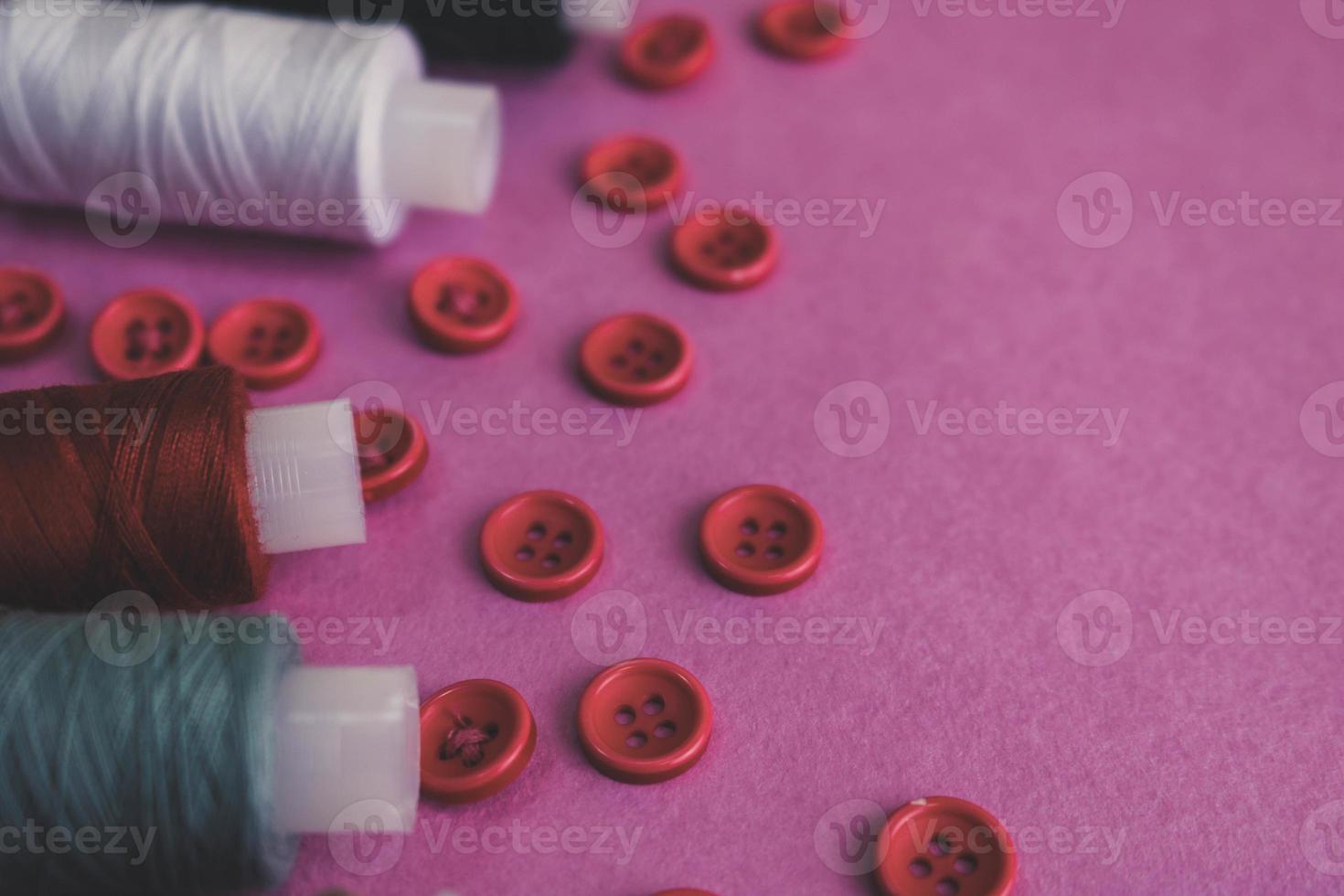 hermosa textura con muchos botones rojos redondos para coser, coser y madejas de carretes de hilo. copie el espacio endecha plana rosa, fondo morado foto