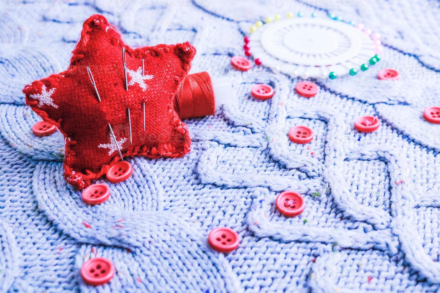 hermosa textura de un suéter natural cálido y suave, telas con un patrón de punto y pequeños botones rojos redondos para coser y una madeja de hilo, cama de aguja y almohadilla de aguja. endecha plana el fondo foto