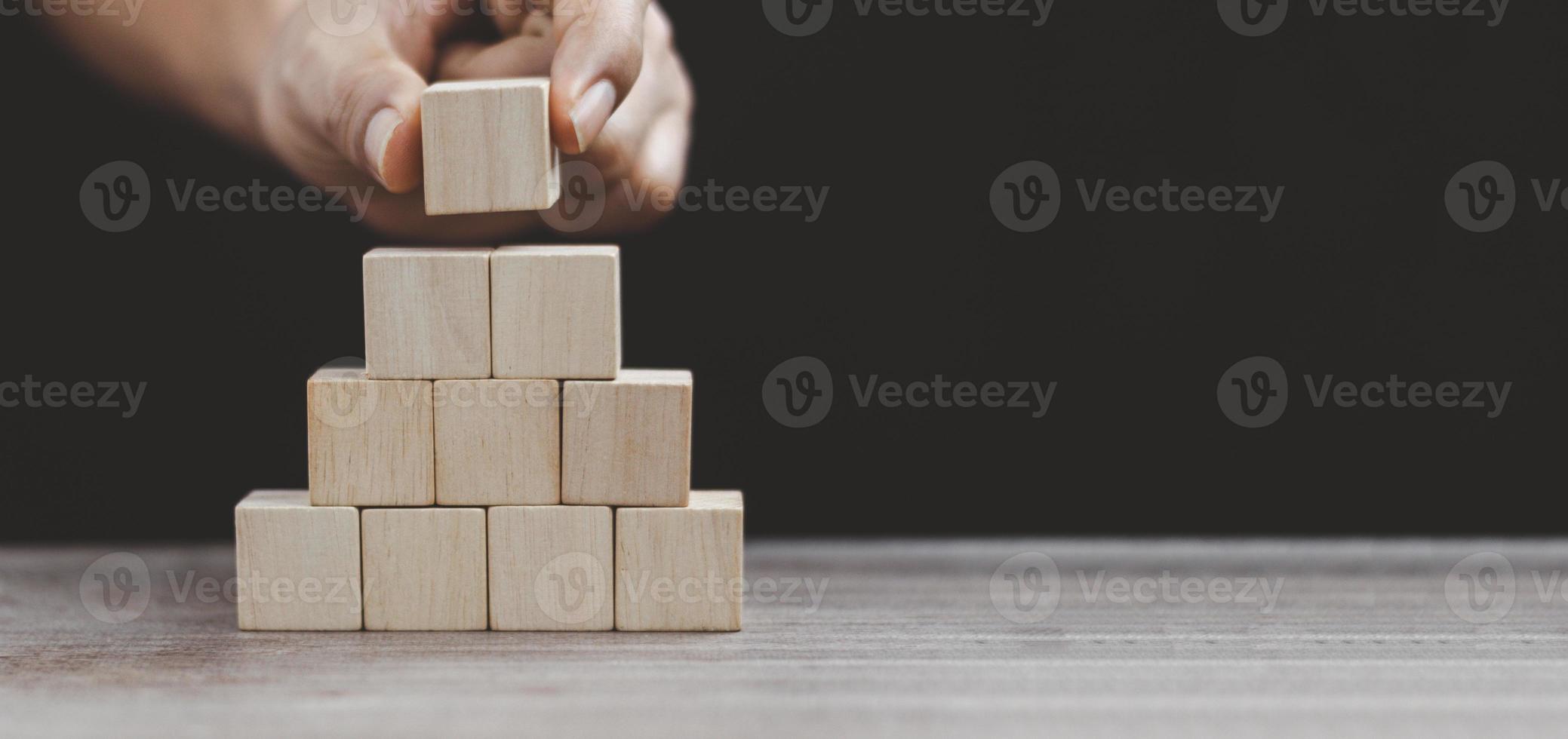 Hand putting wood cube on top of wood block stacking as step stair.business growth to success. photo