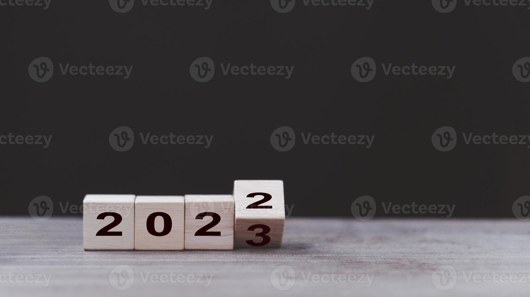 2023 happy new year concept banner. Flipping the 2022 to 2023 year numbers calendar on wooden cube blocks isolated on dark background for new year change for starting new things or new business. photo