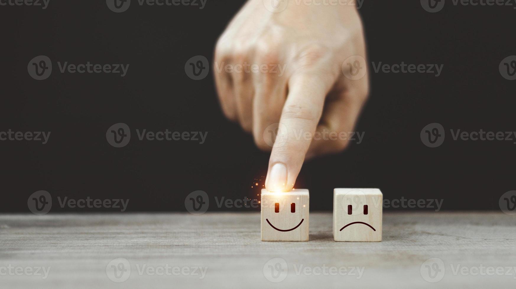 cierre la mano del cliente, elija la cara sonriente y el icono de la cara triste borrosa en el cubo de madera, la calificación del servicio, el concepto de satisfacción. foto