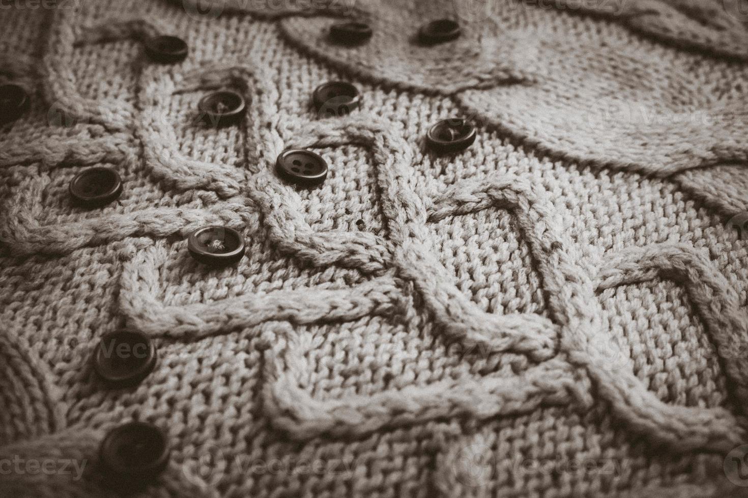 Beautiful texture of a soft warm natural sweater with a knitted pattern of yarn and black and white small round buttons. The background photo