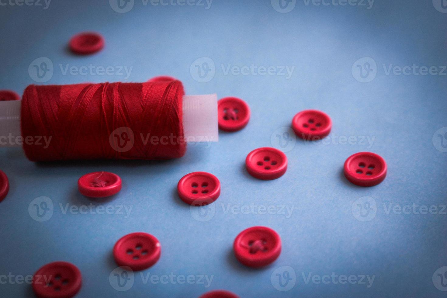 Beautiful texture with lots of round red buttons for sewing, needlework and a coil of thread. Copy space. Flat lay. Blue background photo