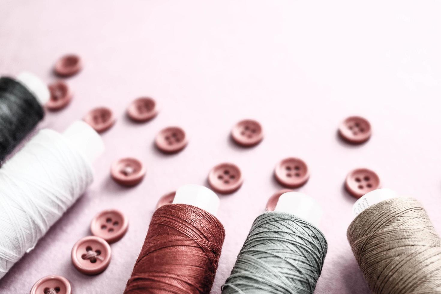 Beautiful texture with lots of round red buttons for sewing, needlework and skeins of spools of thread. Copy space. Flat lay. Pink, purple background photo