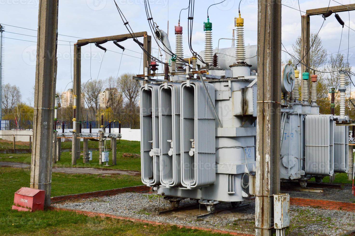 Large industrial iron metal transformer substation with transformers and high-voltage electrical equipment and wires with surge arresters to supply the city with electricity photo