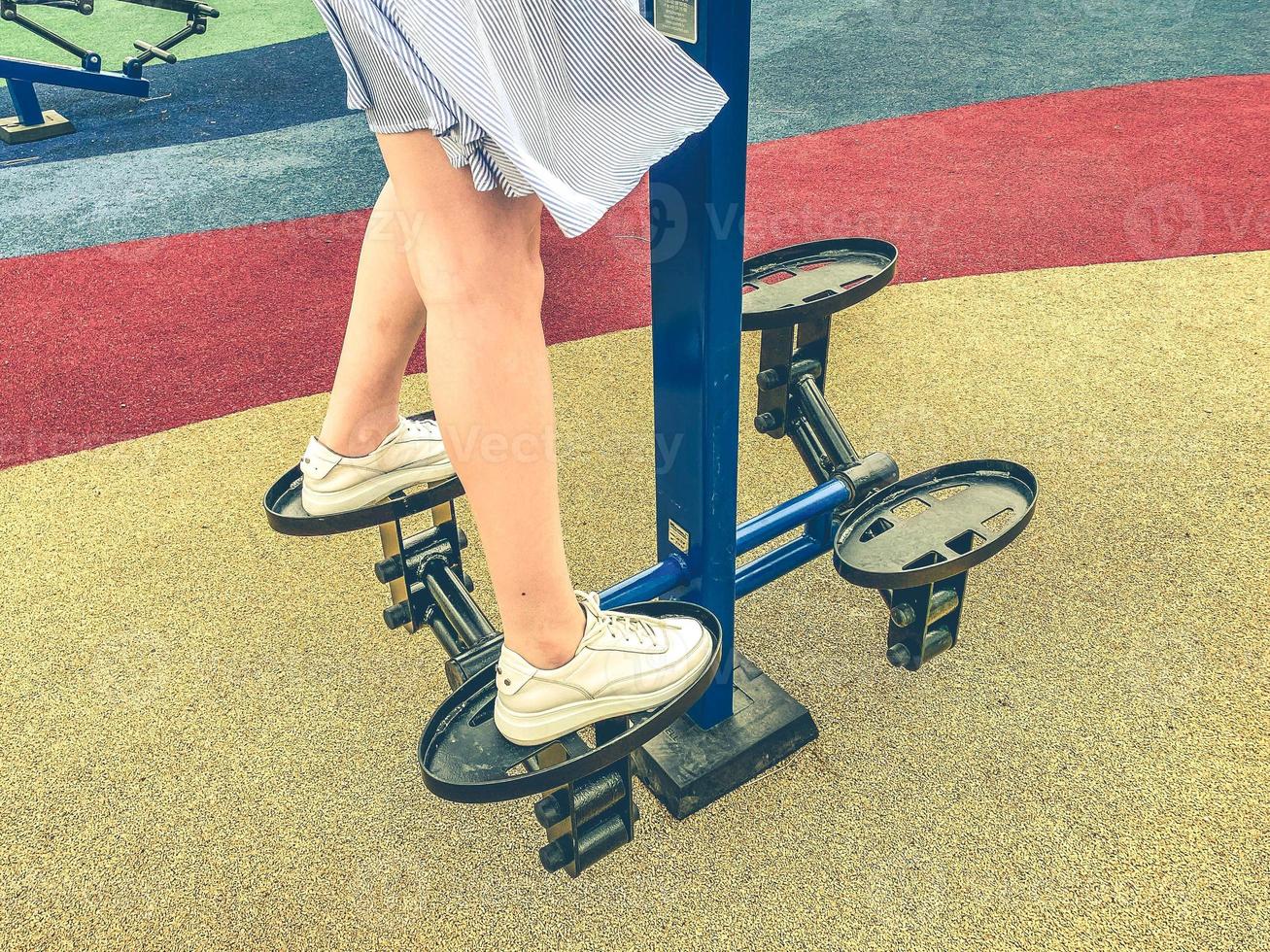 doing sports on the simulator in the park in the fresh air. a girl in a blue dress trains her legs on the platform. athlete in training photo