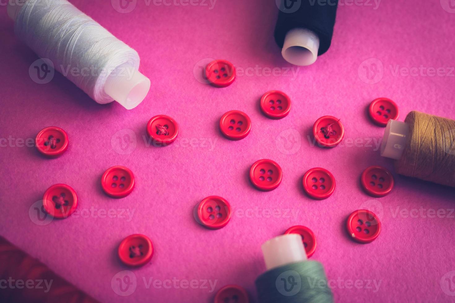 Beautiful frame with a lot of round red buttons for sewing, needlework and skeins of spools of thread. Copy space. Flat lay. Purple pink background photo